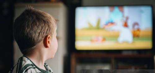 Rear view of cute boy sitting on sofa watching TV